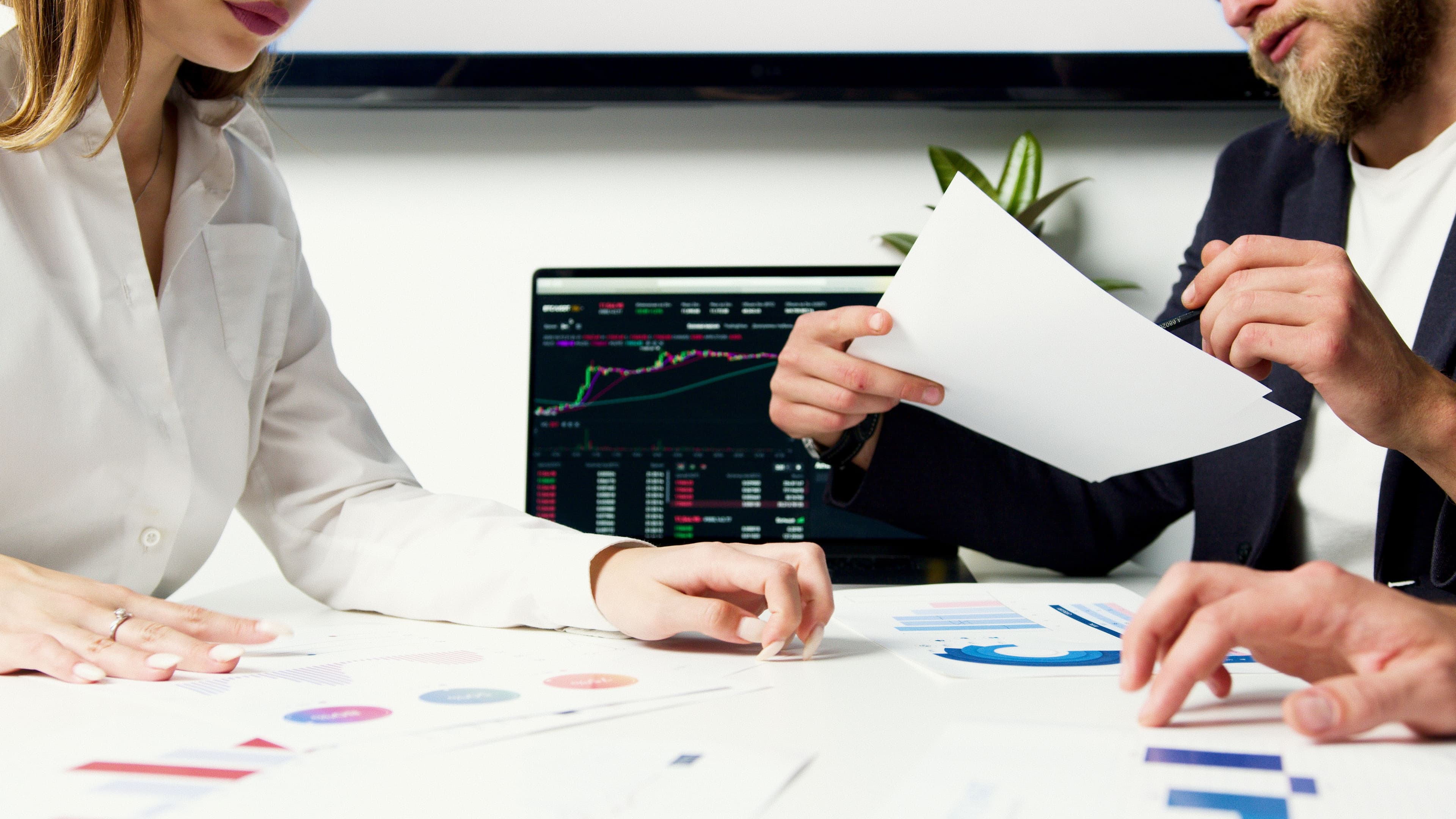 Two Chartered Accountants reviewing printed financial statements and charts beside a laptop showing financial data